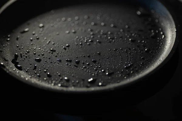 Del av tom gjutjärn stekpanna i svart färg med droppar av vegetabilisk olja. Närbild. Mörk bakgrund. — Stockfoto