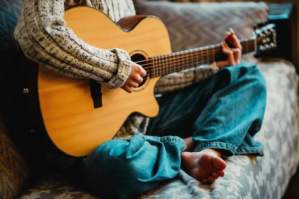 Uzun tırnaklı genç kız evde akustik gitar çalar. Gençler kanepede oturup gitar çalmayı öğrenirler. — Stok fotoğraf