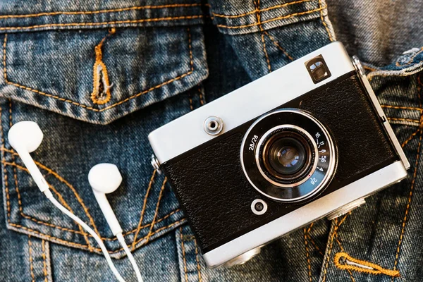 Filmcamera en witte hoofdtelefoon liggen tegen de achtergrond van denim. Modieuze hipster achtergrond. Retrostijl. — Stockfoto