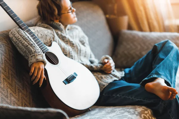 Genç kız kanepede gitar ile oturuyor. Ergen, müzik aleti olan bir hipster.. — Stok fotoğraf