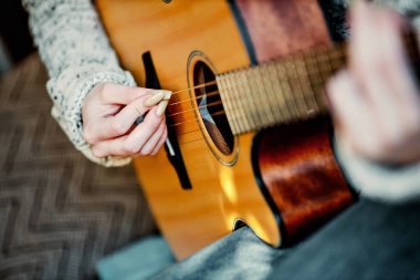 Uzun tırnaklı genç kız evde akustik gitar çalar. Gençler kanepede oturup gitar çalmayı öğrenirler.