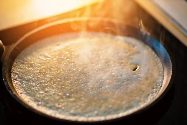 A palacsintát fekete öntöttvas serpenyőben sütik, és füst van benne. Ízletes hagyományos desszert készítése otthon. — Stock Fotó