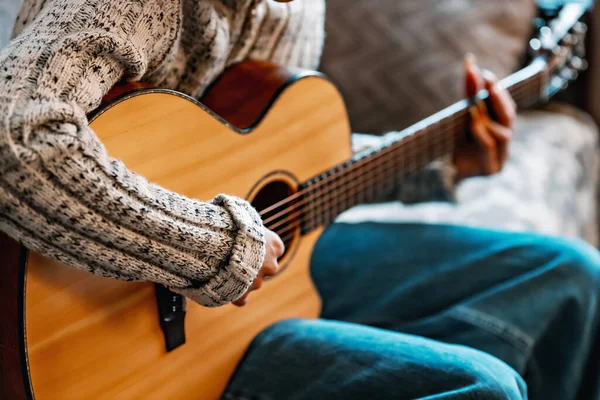 Uzun tırnaklı genç kız evde akustik gitar çalar. Gençler kanepede oturup gitar çalmayı öğrenirler. — Stok fotoğraf