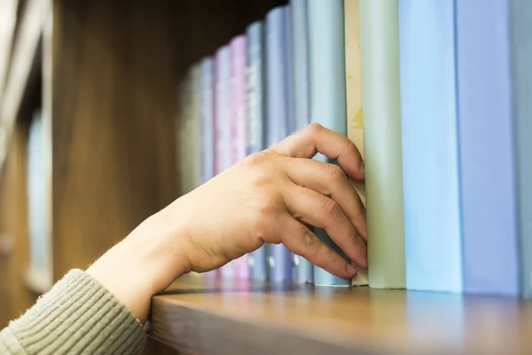 Mano sacando un libro de la estantería —  Fotos de Stock