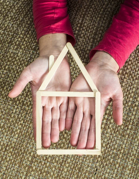 Mani che tengono casa modello fatta di bastoni di legno — Foto Stock