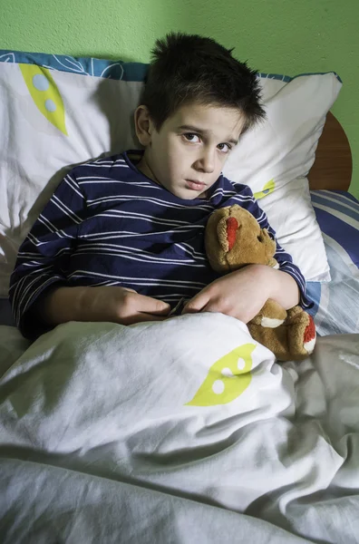 Больной ребенок в постели с плюшевым мишкой — стоковое фото
