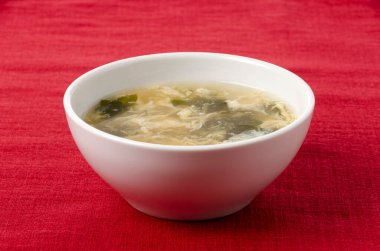 wakame yosun yumurtası çorbası beyaz kasede kırmızı bez arka planda düşer.