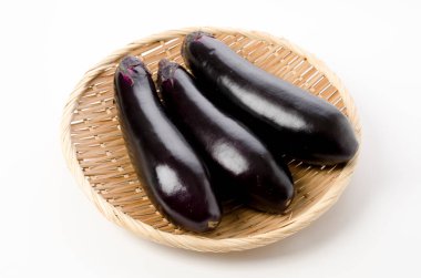 Beyaz arka planda bambu elek üzerinde taze siyah patlıcan.