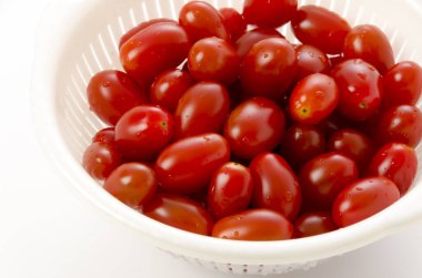 Beyaz arka planda plastik bir süzgeçte taze kiraz domatesleri.