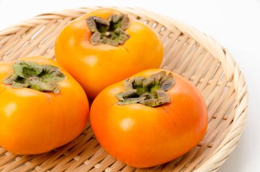 Kaki, beyaz arka planda bambu elek üzerine hurma meyvesi.