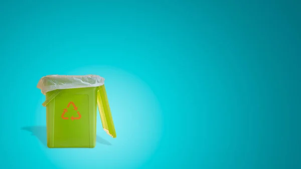 Banner with a green garbage trash bin with bag inside with its shadow and recycling symbol at turquoise gradient background with copy space. Concept of waste recycling