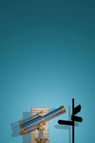 Cover page with old antique metal telescope standing near a stack of books with a post showing directions at gradient blue background with copy space and shadow. Concept exploration, education, travel