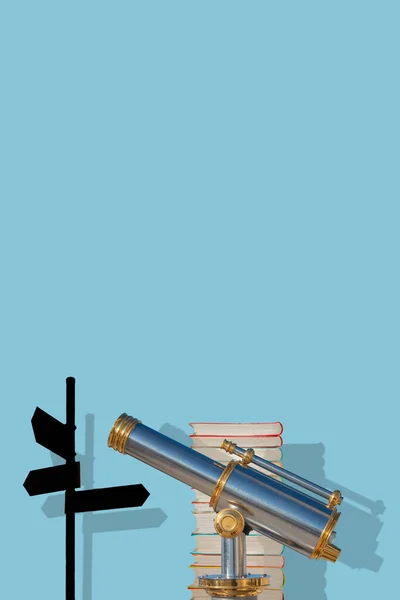 Cover page with an old antique metal telescope standing near a stack of books with a post showing directions at solid blue background with copy space and shadow. Concept exploration, education and travel