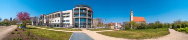 Magdeburg, Almanya - 9 Mayıs 2021: Alışveriş merkezi Allee Center 'ın panoramik manzarası, çiçek açan kiraz ağacı ve mavi bahar gökyüzünde Magdeburg şehir merkezinde bulunan Aziz Jochannis Kilisesi (Jochanniskirche)