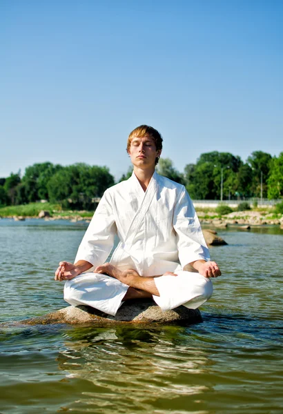 Homem de quimono meditando sobre a rocha no mar — Fotografia de Stock