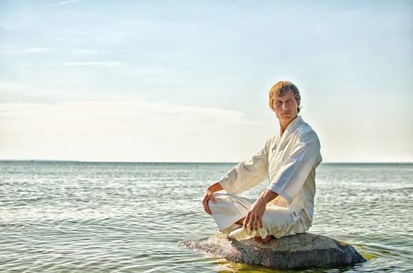 Man in kimono meditating on the rock in the sea — Stock Photo, Image