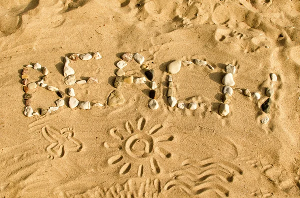 Woord strand gemaakt van stenen op het zand. — Stockfoto