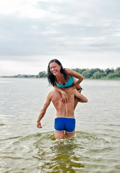 海で肩に女性を運んでいる男 — ストック写真