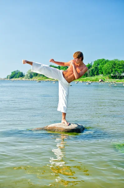 Hombre en kimono entrenando en la roca en el mar Imagen de archivo