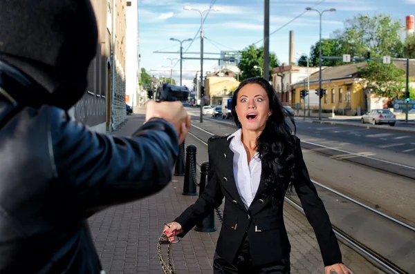 Bandita s zbraň ohrožuje mladou ženou na ulici — Stock fotografie