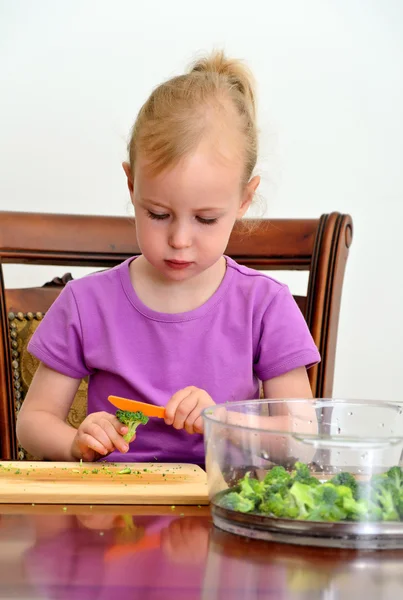 Liten flicka skär broccoli i köket — Stockfoto