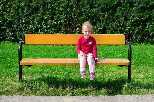 Liten flicka sitter på bänken i parken — Stockfoto