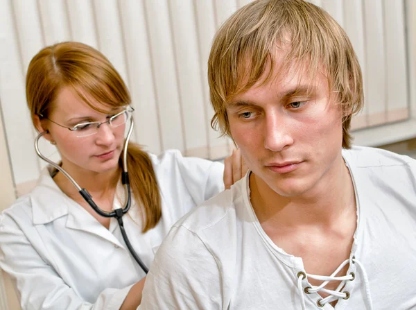 年轻的女医生用听诊器检查男性病人。以病人为中心 — 图库照片