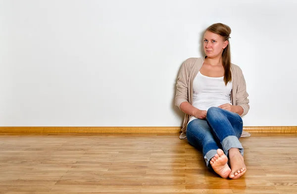 Молодая женщина сидит на деревянном полу напротив белой стены — стоковое фото