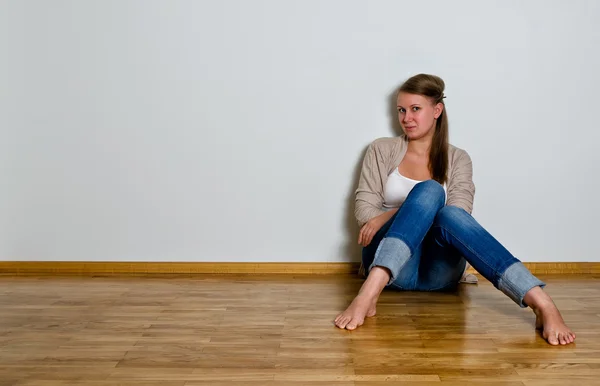 Jeune femme assise sur le sol en bois contre un mur blanc — Photo