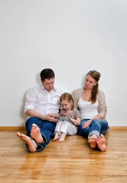 Famille heureuse assis sur le sol contre le mur et en utilisant la tablette calculer — Photo