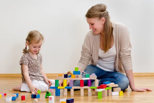 Söt liten flicka och ung kvinna sitter på golvet och leker med Bygg — Stockfoto