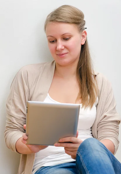 Mladá žena sedí proti zdi a použití tabletového počítače — Stock fotografie