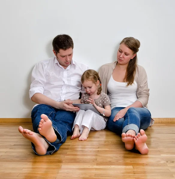 Familia feliz sentado en el suelo contra la pared y el uso de la tableta computar —  Fotos de Stock