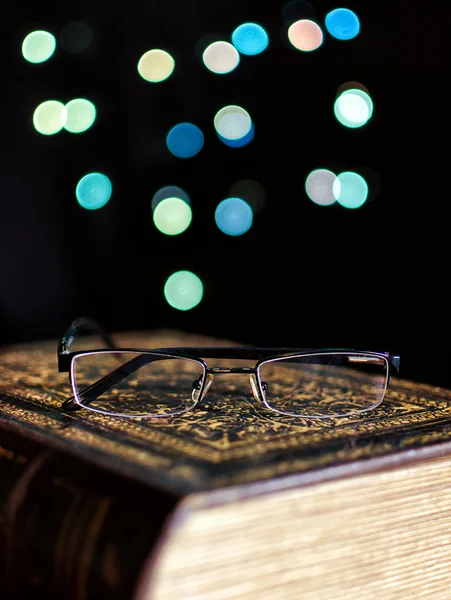 Libro viejo y gafas sobre fondo de luces bokeh — Foto de Stock