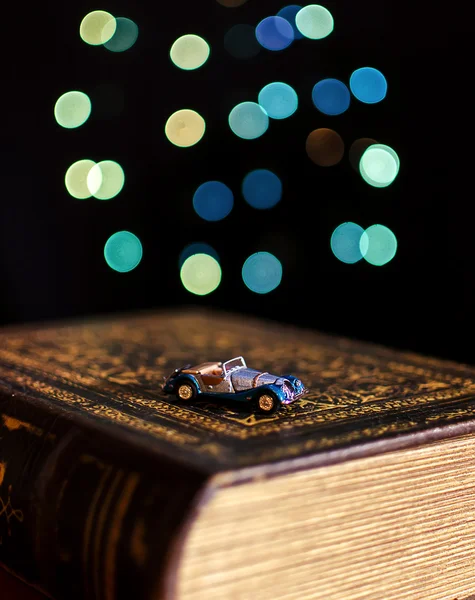 Livro velho e carro em miniatura no fundo luzes bokeh — Fotografia de Stock