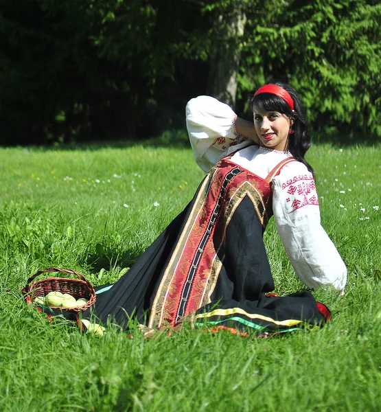 Pretty woman in russian traditional costume sitting on the grass — Stock Photo, Image