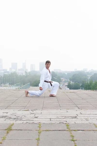 Giovane maestro di karate che fa esercizio n la mattina sullo sfondo della città — Foto Stock