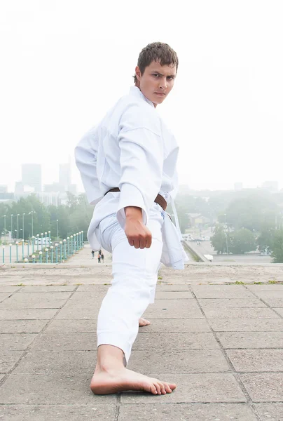 Giovane maestro di karate che fa esercizio n la mattina sullo sfondo della città — Foto Stock