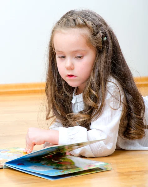 Mooi klein meisje op de vloer liggen en lezen van een boek — Stockfoto