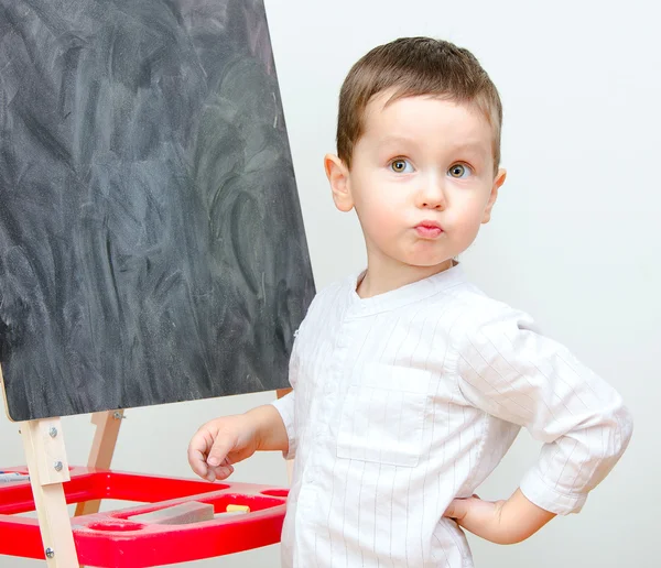 Liten pojke står nära blackboard — Stockfoto