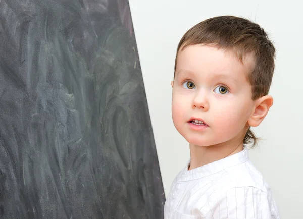 Pequeño niño de pie cerca de pizarra — Foto de Stock