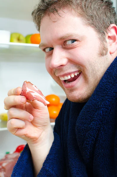 Bell'uomo che va a mangiare prosciutto vicino al frigo aperto — Foto Stock