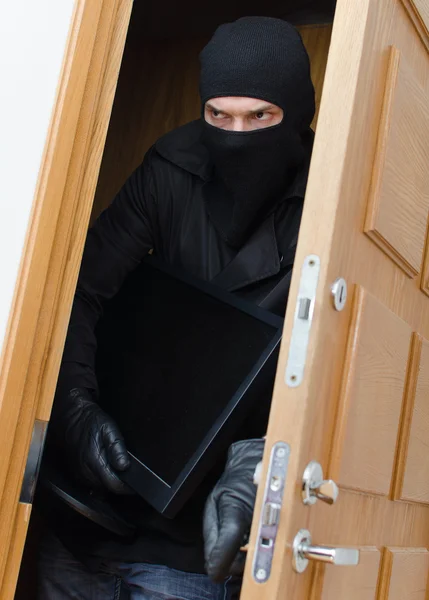Male burglar in mask breaking into the house and stealing monitor — Stock Photo, Image
