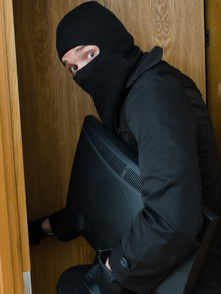 Male burglar in mask breaking into the house and stealing monitor — Stock Photo, Image