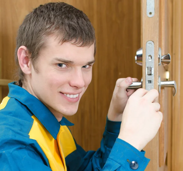 Uśmiechający się złota rączka w mundurze wymiana zamka drzwi — Zdjęcie stockowe
