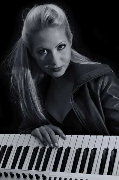 Sexy lady in bra and leather coat posing with synthesizer. Black and white — Stock Photo, Image