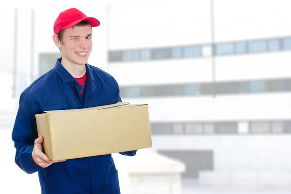 Young smiling courier holding cardboard box on urban building background — Stock Photo, Image