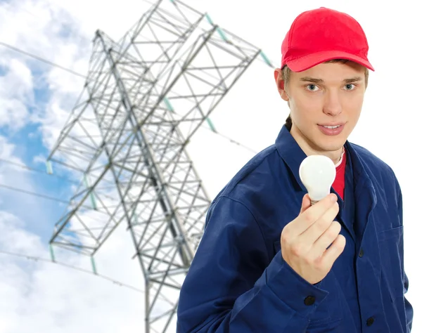 Jovem eletricista em uniforme com lâmpada no fundo da torre de transmissão — Fotografia de Stock