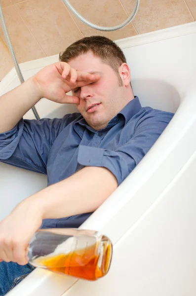 Пьяный мужчина с бутылкой, лежащий в ванной — стоковое фото