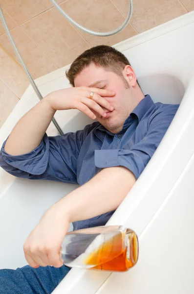 Drunk man with bottle lying in bath — Stock Photo, Image